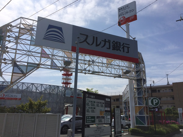 道を挟んで反対側にスルガ銀行、ダイレクトワンの看板が出ている建物がございますので、敷地内に進んでください。